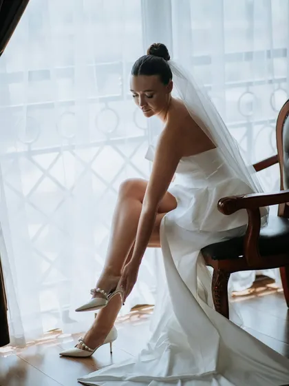 The final touch. A bride adjusts her pearl-adorned shoes, a small detail that tells a big part of her love story as she prepares to walk into forever.