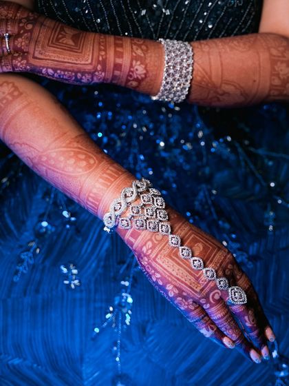 An artistic shot highlighting the bride's diamond hand harness (hathphool) against her dark blue gown and intricate mehndi. The lighting makes the jewelry pop.