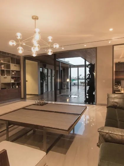 A modern living room with an open connection to an outdoor terrace. The space features a contemporary chandelier, a comfortable leather sofa, and a neutral color palette, creating a warm and inviting environment.