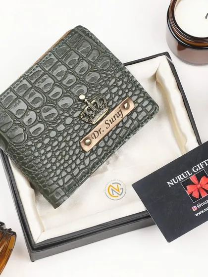 A personalized wallet in an olive green crocodile leather finish, featuring a crown charm and a 'Dr.' title on the nameplate.
