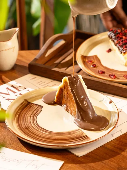 The final touch of pouring warm chocolate sauce over a cheesecake, creating a glossy, decadent finish.