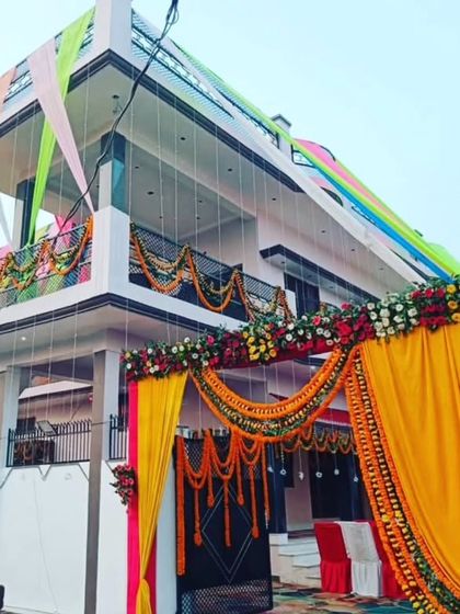 A grand entrance decoration for a wedding house. The gate is decorated with a large arch of yellow and pink drapes and flowers, and the house facade is also adorned with colorful fabric.