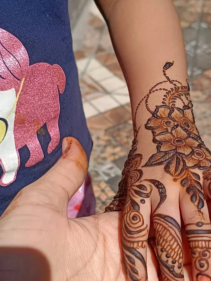 Here is a clear look at a classic floral mehendi design on the back of a child's hand. I'm holding her hand to show the scale and detail of the flower and leaf patterns that extend down the fingers. This is a very popular choice for parties.