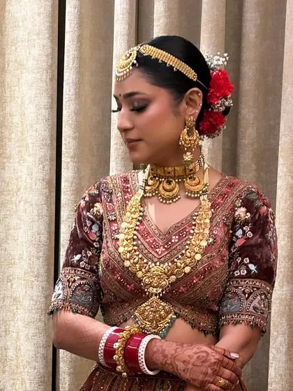 A beautiful bridal updo with a traditional matha patti and bright red flowers. This is a classic North Indian bridal look that is vibrant and celebratory.