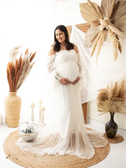 An angelic look in all white. This studio setup with a disco ball and pampas grass creates a bohemian-chic vibe for a serene maternity portrait.