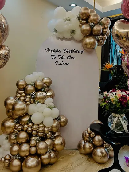 A close-up of the birthday backdrop, showing the mix of chrome gold and white balloons, a fresh flower bouquet, and heart-shaped foil balloons.