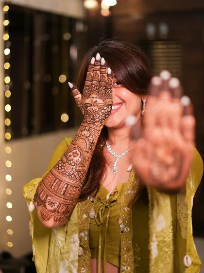 A happy smile and a hand full of henna. This bride is playfully showing off her full-arm mehendi, a beautiful mix of traditional patterns and personalized story elements.