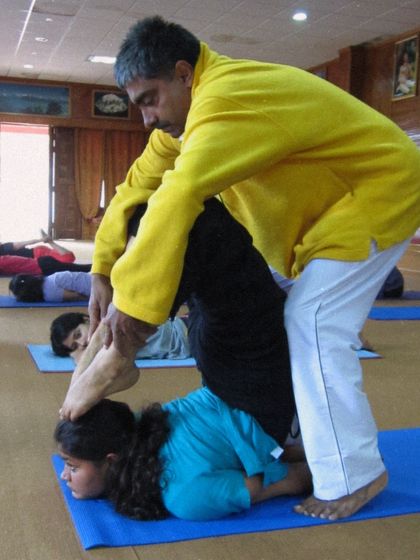 A teacher assists a student in Salabhasana, the locust pose, to build back strength. This demonstrates the supportive and educational nature of our training.
