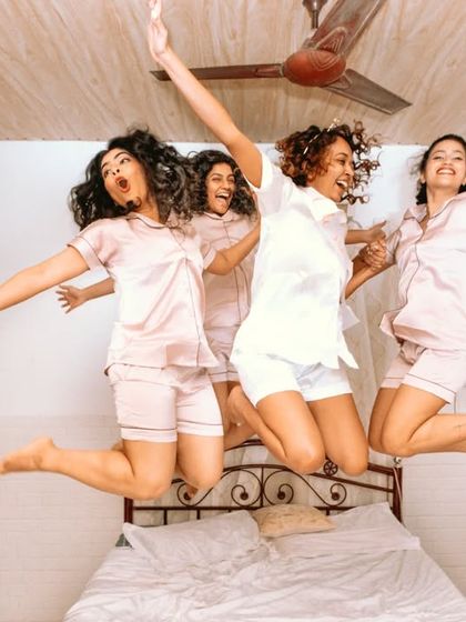 Girl power! The bride and her bridesmaids jump for joy on the bed, a moment of pure fun and friendship.