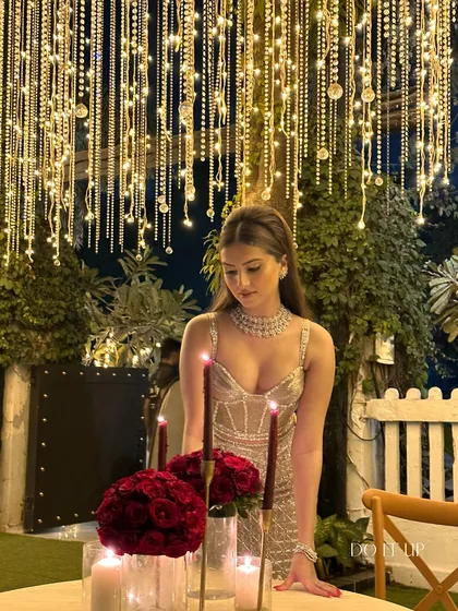 A glamorous birthday celebration. A canopy of cascading string lights creates a sparkling, starlit effect over the dinner table, which is set with deep red roses and candles for an intimate and luxurious feel.