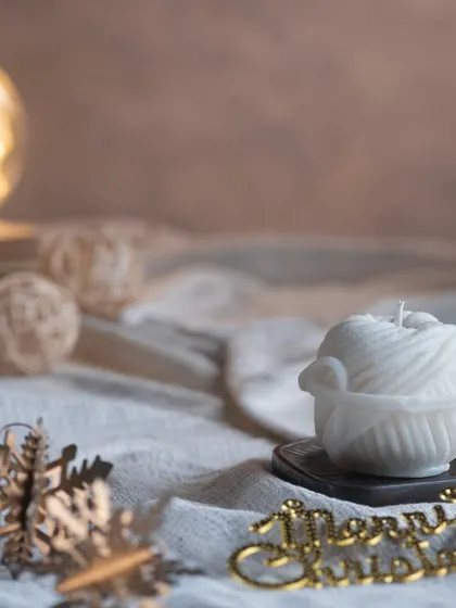 A uniquely designed candle shaped like a ball of yarn in a basket. It's a perfect, cozy gift for someone who loves knitting or crafting.