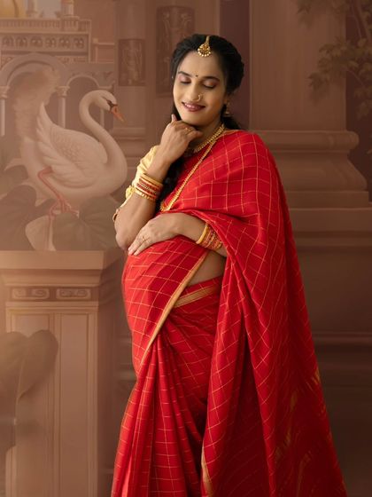 A lovely portrait of a mom-to-be in a red saree, gently holding her baby bump with a serene expression.
