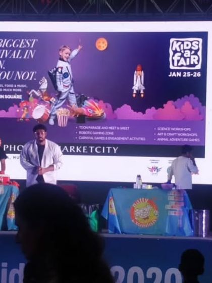 Our professors command the stage, explaining the science behind the spectacle. This view shows our setup in front of a large screen at a major kids' fair, highlighting the scale of our performances.