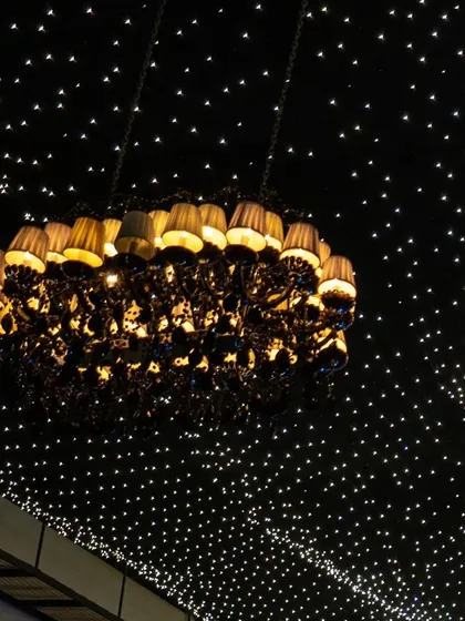 A grand lampshade chandelier hangs like a piece of art against a ceiling of twinkling fairy lights.