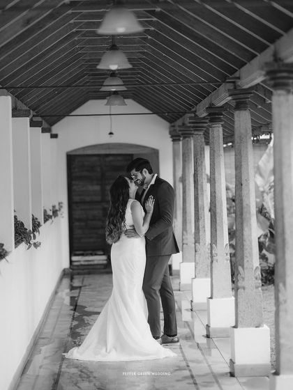 A classic black and white shot of Akshatha and Jeethesh sharing a kiss in a traditional corridor. The architecture perfectly frames this romantic moment.