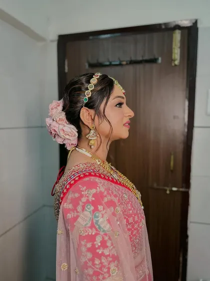 A classic bridal bun made romantic with a garland of fresh pink roses. This style is perfect for the main ceremony, keeping the hair elegantly off the face while adding a soft, floral touch to the overall look.