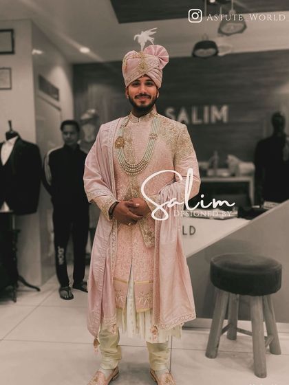 This groom is wearing a pastel pink sherwani with delicate embroidery. The look is completed with a matching safa and a multi-strand pearl necklace, perfect for a daytime wedding.