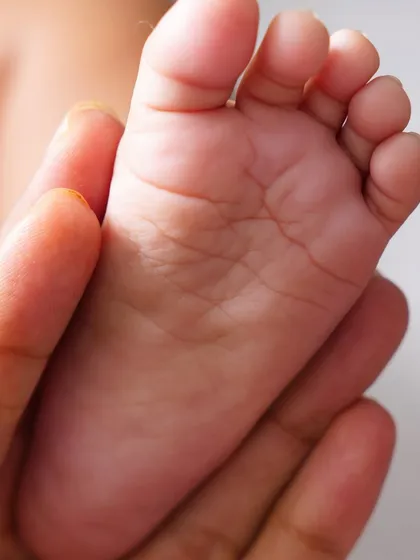 Capturing the tiniest details. A close-up shot of a newborn's tiny foot being held gently in a parent's hand.