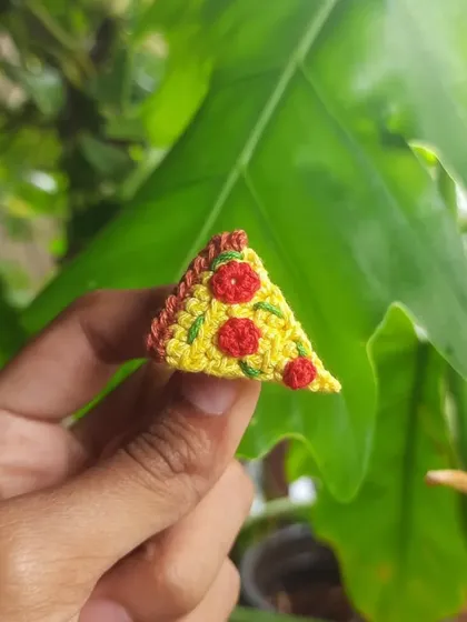 A tiny slice of pepperoni pizza, made into a pin or charm. It's a perfect little accessory for any food lover.