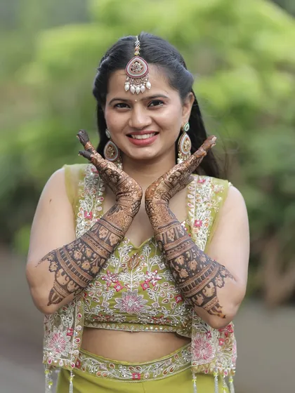A joyful bride, her hands framing her beautiful smile. The mehendi is a stunning complement to her bridal glow.