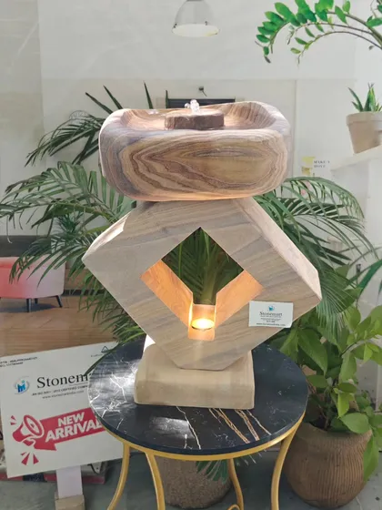 This 19-inch tall tabletop fountain combines a stone lamp and a water feature. The warm light from within highlights the natural patterns of the rainbow sandstone, creating a soothing ambiance.