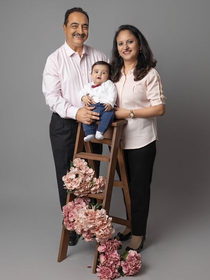 Grandparents posing with their grandchild, who is perched on a small ladder decorated with flowers. Using simple props can add a touch of creativity to family portraits.