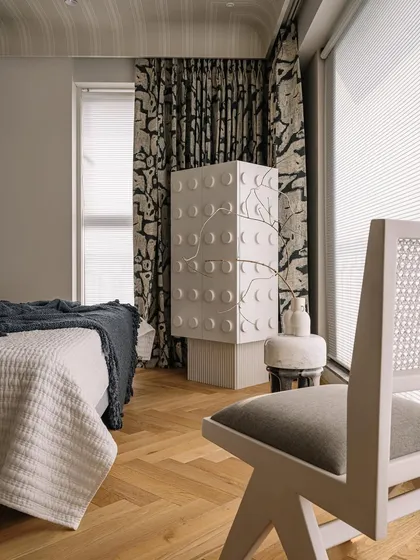 In the master bedroom, a custom-designed cabinet with a tree motif adds a sculptural and artistic element. The bold wallpaper on the ceiling is an unexpected and delightful detail.