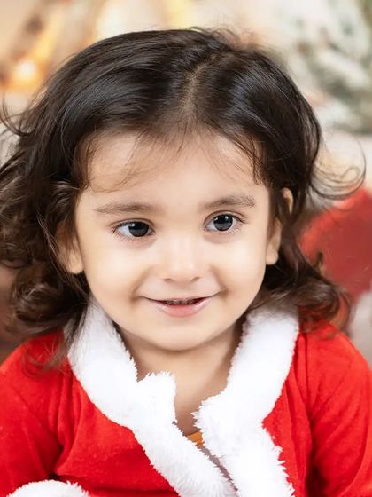 A close-up of a smiling toddler girl in her Santa suit, her eyes sparkling with holiday magic.