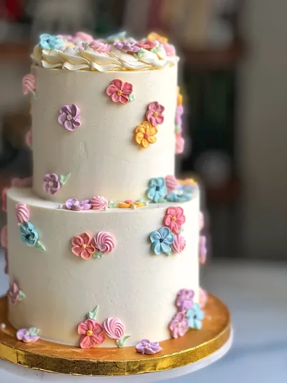 This two-tiered cake is decorated with a cascade of small, hand-piped buttercream flowers in a variety of pastel colors. It's a sweet and whimsical design perfect for a kid's birthday.