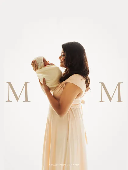 A creative and minimalist portrait celebrating motherhood. A new mother holds her baby against a clean, white background with the word 'MOM' framing the tender moment.