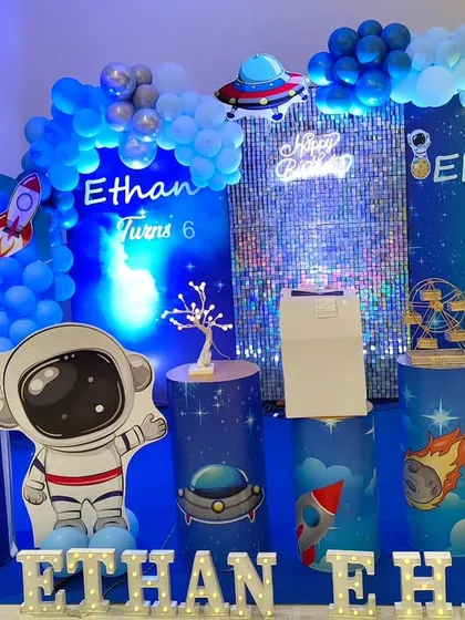 An out-of-this-world space and astronaut theme for a joint birthday party. This design uses cool blue lighting, a sparkling sequin wall, and themed props like astronauts, rockets, and a crescent moon to create a cosmic adventure.