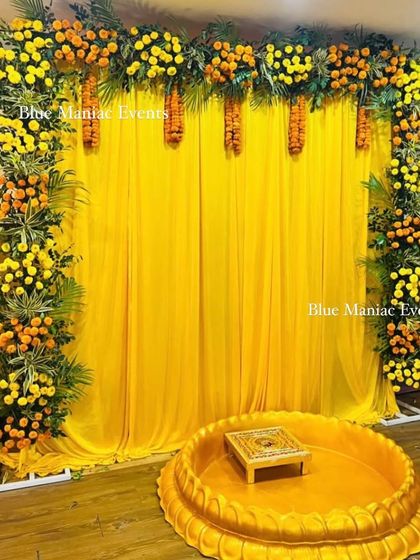 A classic Haldi setup with a backdrop of yellow drapes and a frame of marigolds and green leaves, complete with a traditional urli.