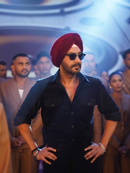 A powerful shot of Ajay Devgn as Jassi in a key song sequence. The all-black ensemble with a contrasting deep red turban creates a commanding and heroic silhouette. This look was designed for high visual impact on screen.