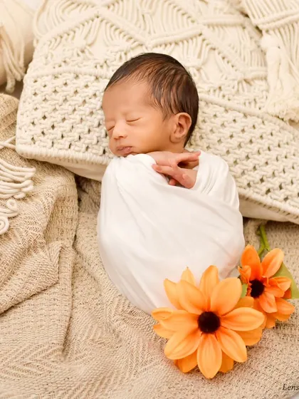 This portrait showcases a boho-inspired setup with macrame textures and warm, earthy tones. The baby is peacefully asleep, wrapped snugly in white, creating a serene and stylish image.
