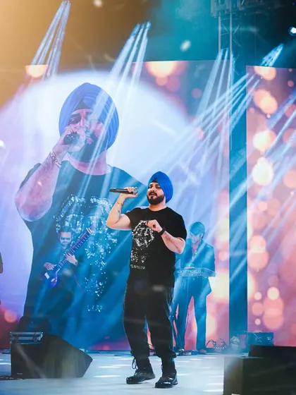 A wide shot of Manmeet Singh performing, with his image projected on the large screen behind him, creating a larger-than-life concert photograph.
