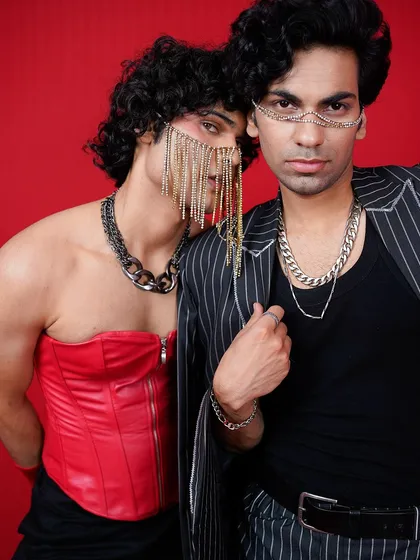 This conceptual editorial shoot explores themes of connection and identity. The bold red background, striking chain-link face jewelry, and the models' intense interaction create a visually arresting image that is both artistic and thought-provoking.