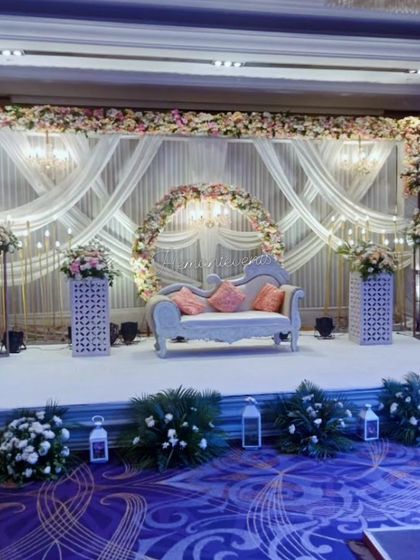An elegant indoor stage for a ring ceremony or reception. The backdrop features beautiful white drapes, a floral arch, and chandeliers, creating a classic and sophisticated look.