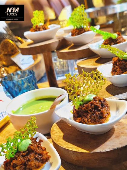 A rich and savory appetizer, beautifully presented with a crispy garnish and a side of green chutney. The multi-level wooden server adds a rustic yet sophisticated touch.