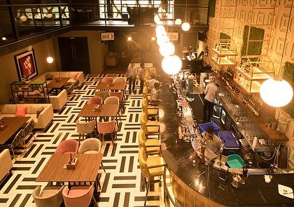 An overhead view of the bar and dining floor at Dank. The strategic placement of plants helps to define different zones and adds visual interest to the geometric floor pattern.