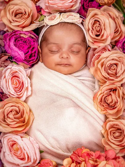 Pure and simple beauty. This close-up shot captures a sleeping newborn's delicate features, framed by a bed of soft pink and peach roses. It's a timeless portrait that celebrates the gentle innocence of a new baby.