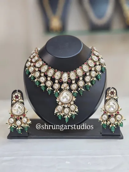 A classic and elegant Kundan bridal set that never goes out of style. This necklace and earring set features large, uncut polki-style stones, beautifully contrasted with deep green and ruby-red beads. It's a versatile choice that complements a wide range of bridal lehengas and sarees.