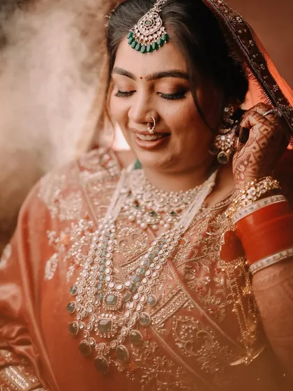 A close-up shot of the bride adjusting her earring. This candid-style portrait captures a quiet, personal moment of getting ready, focusing on the intricate details of her jewelry and her serene expression.