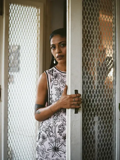 A close-up of Anasuya Sengupta peering through a screen door. The mesh adds texture and a layer of separation, making the portrait more intriguing.