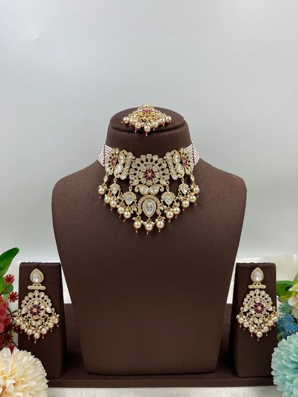 The Ziva Premium Moissanite Kundan Necklace. This choker set is defined by its floral-inspired motifs, pearl droppings, and a matching maang tikka, available in both red and green stone options.