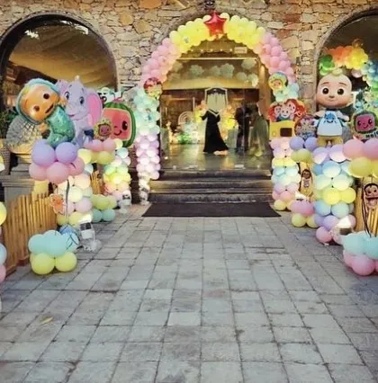 A grand Cocomelon entrance for an outdoor party, with giant inflatable characters and balloon pillars lining the walkway.