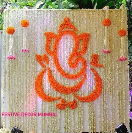 This stunning backdrop features a Ganpati motif skillfully crafted from orange marigolds against a curtain of white jasmine strings. The hanging floral tassels add an extra layer of detail and tradition.
