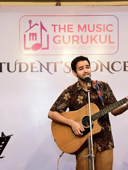 An adult student performs with his acoustic guitar at the TMG Student's Concert. Our community includes learners of all ages, all sharing a passion for music.