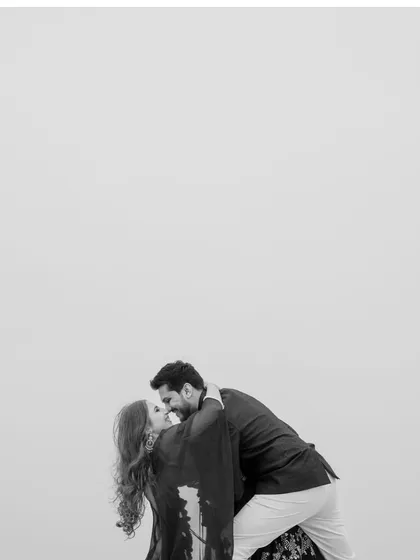 A minimalist black and white portrait of Priyangi and Kishan sharing a kiss against a stark sky. The simplicity of the composition puts all the focus on their love and intimacy.