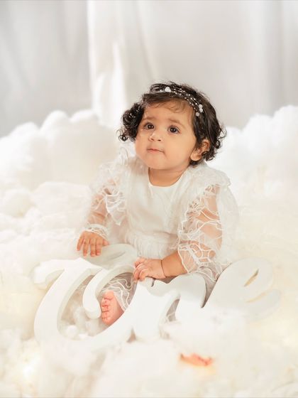 This little one is holding a "One" sign, marking her very first birthday in this heavenly cloud-themed photoshoot.