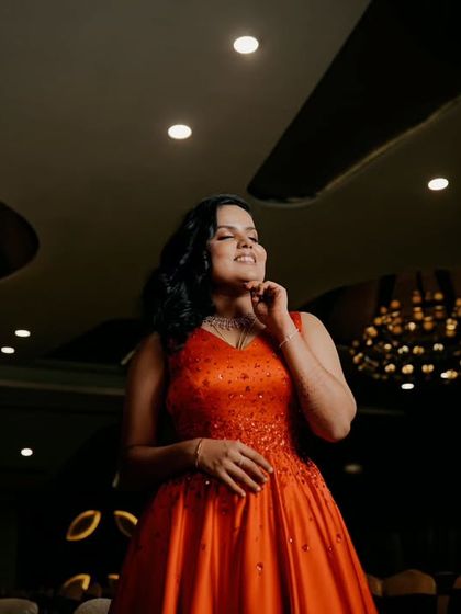 A solo portrait of the bride at her reception, looking radiant in her vibrant orange gown against the dark, elegant backdrop of the hall.